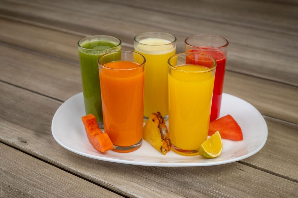 Colorful array of fresh fruit juices in glasses on a white plate with assorted fruits.